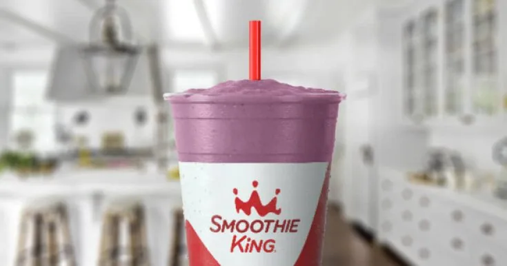 Smoothie King Power Meal Blueberry Raspberry smoothie in a glass, on my kitchen counter, surrounded by fresh blueberries and raspberries.