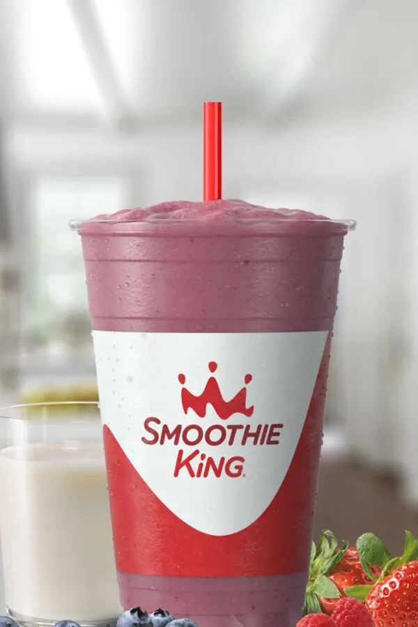 Smoothie King Vegan Mixed Berry smoothie in a glass, on my kitchen counter, surrounded by fresh berries and a glass of oat milk.