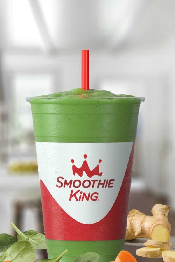 Smoothie King Veggie Lemon Ginger Spinach smoothie in a glass, on my kitchen counter, surrounded by fresh spinach and ginger.