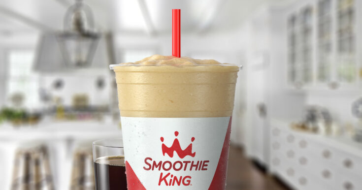 Smoothie King Coffee D-Lite Vanilla smoothie in a glass, on my kitchen counter, surrounded by coffee beans.