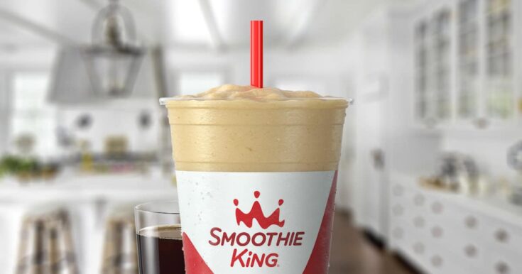 Smoothie King Espresso D-Lite Vanilla smoothie in a glass, on my kitchen counter, surrounded by coffee beans.