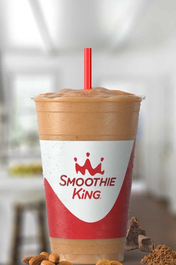 Smoothie King Espresso High Protein Almond Mocha smoothie in a glass, on my kitchen counter, surrounded by almonds and chocolate.