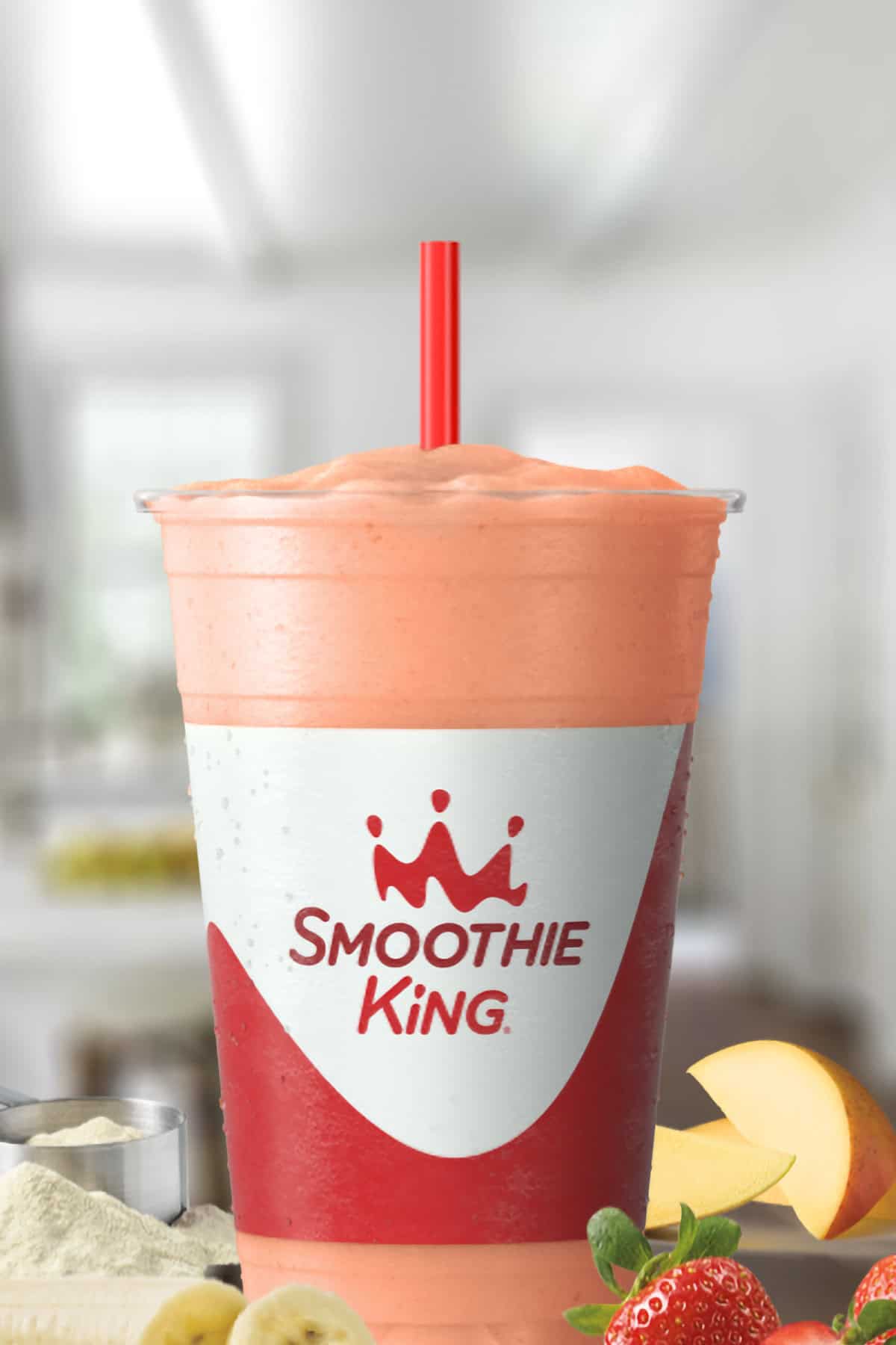 Smoothie King Kindness In A Cup smoothie in a glass, on my kitchen counter, surrounded by fresh fruit and whey protein powder.