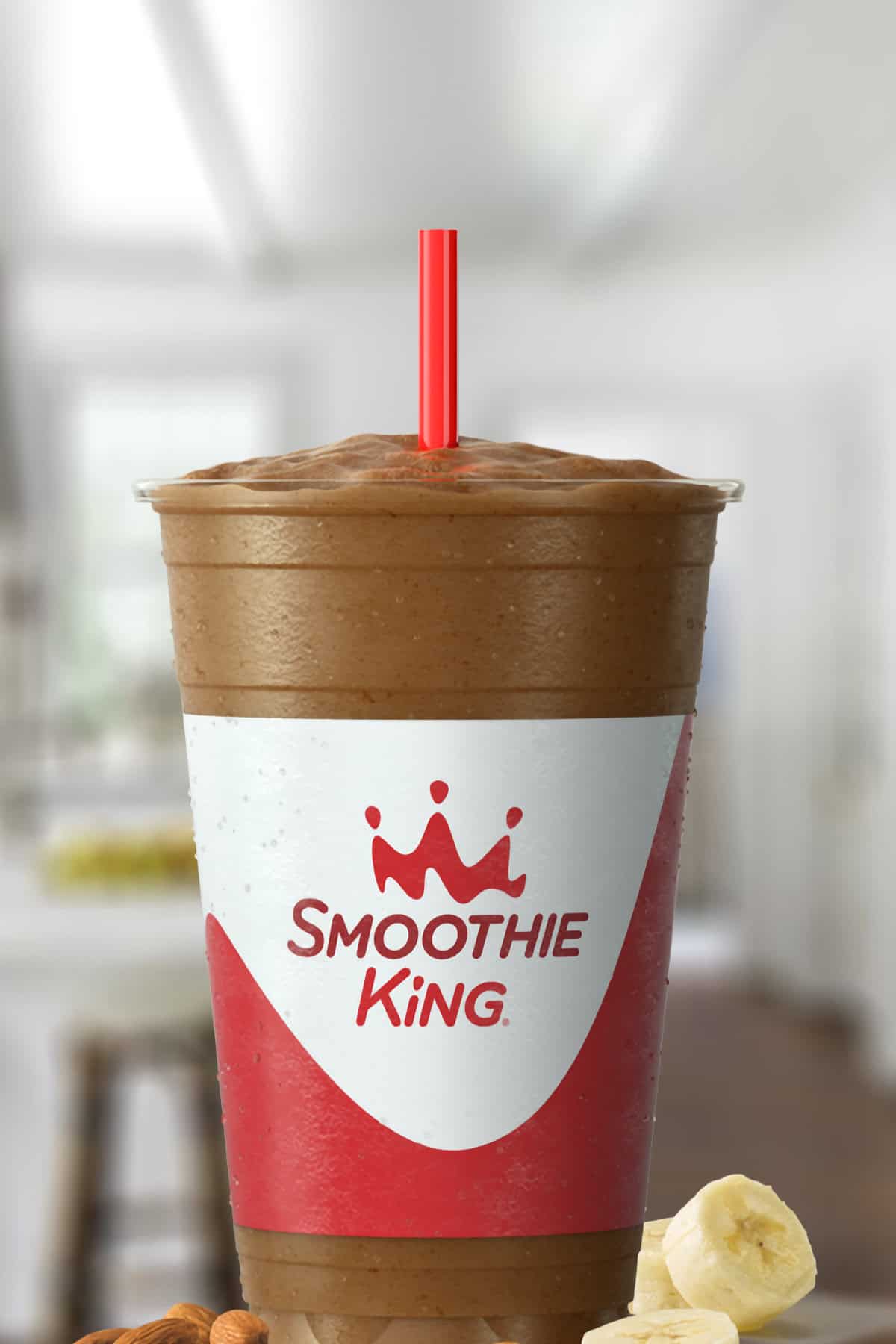 Smoothie King Lean1 Chocolate smoothie in a glass, on my kitchen counter, surrounded by almonds and banana slices.