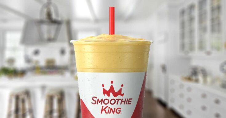 Smoothie King Lean1 Pineapple Mango smoothie in a glass, on my kitchen counter, surrounded by pineapple slices and mango.