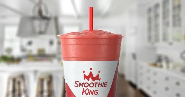 Smoothie King Muscle Punch smoothie in a glass, on my kitchen counter, surrounded by fresh strawberries and bananas.