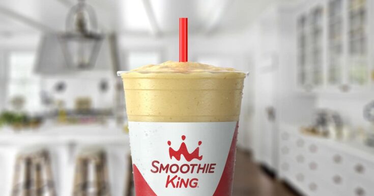 Smoothie King Original High Protein Banana smoothie in a glass, on my kitchen counter, surrounded by banana slices.