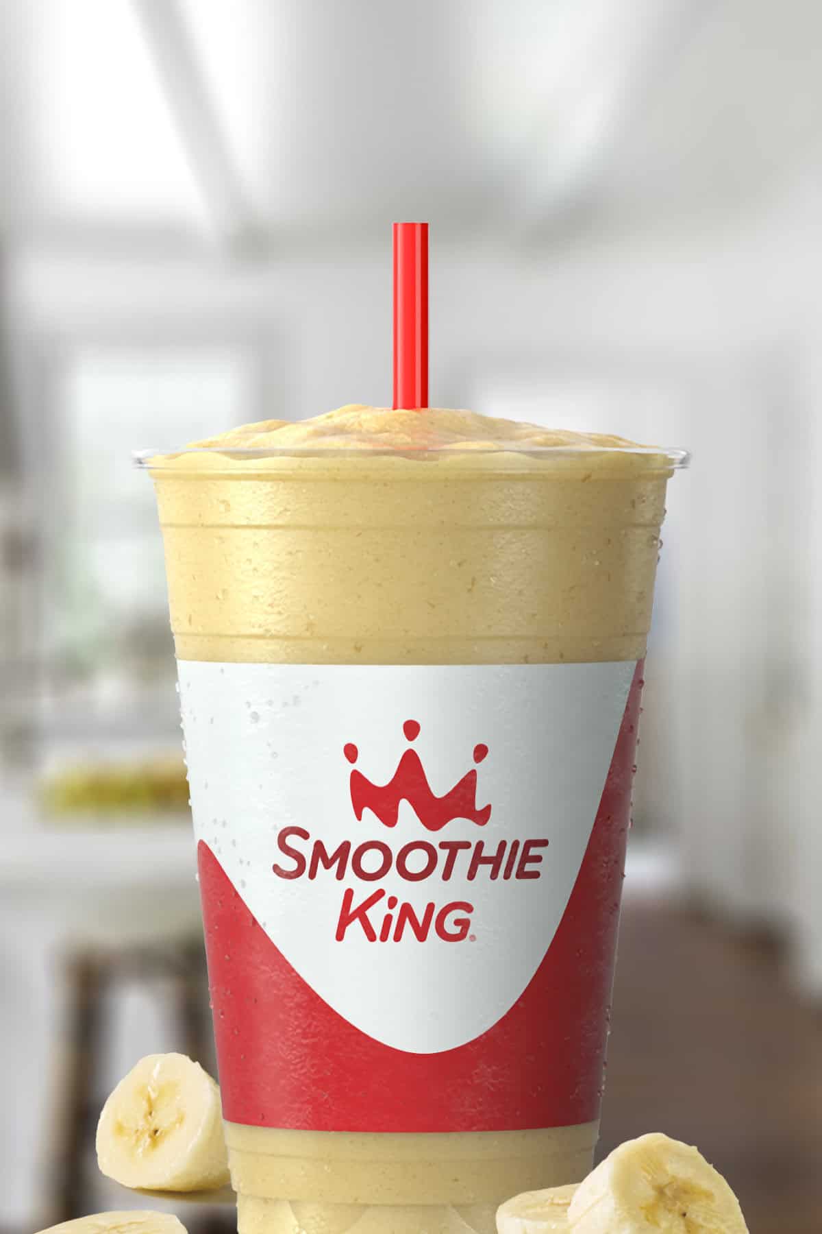 Smoothie King Original High Protein Banana smoothie in a glass, on my kitchen counter, surrounded by banana slices.