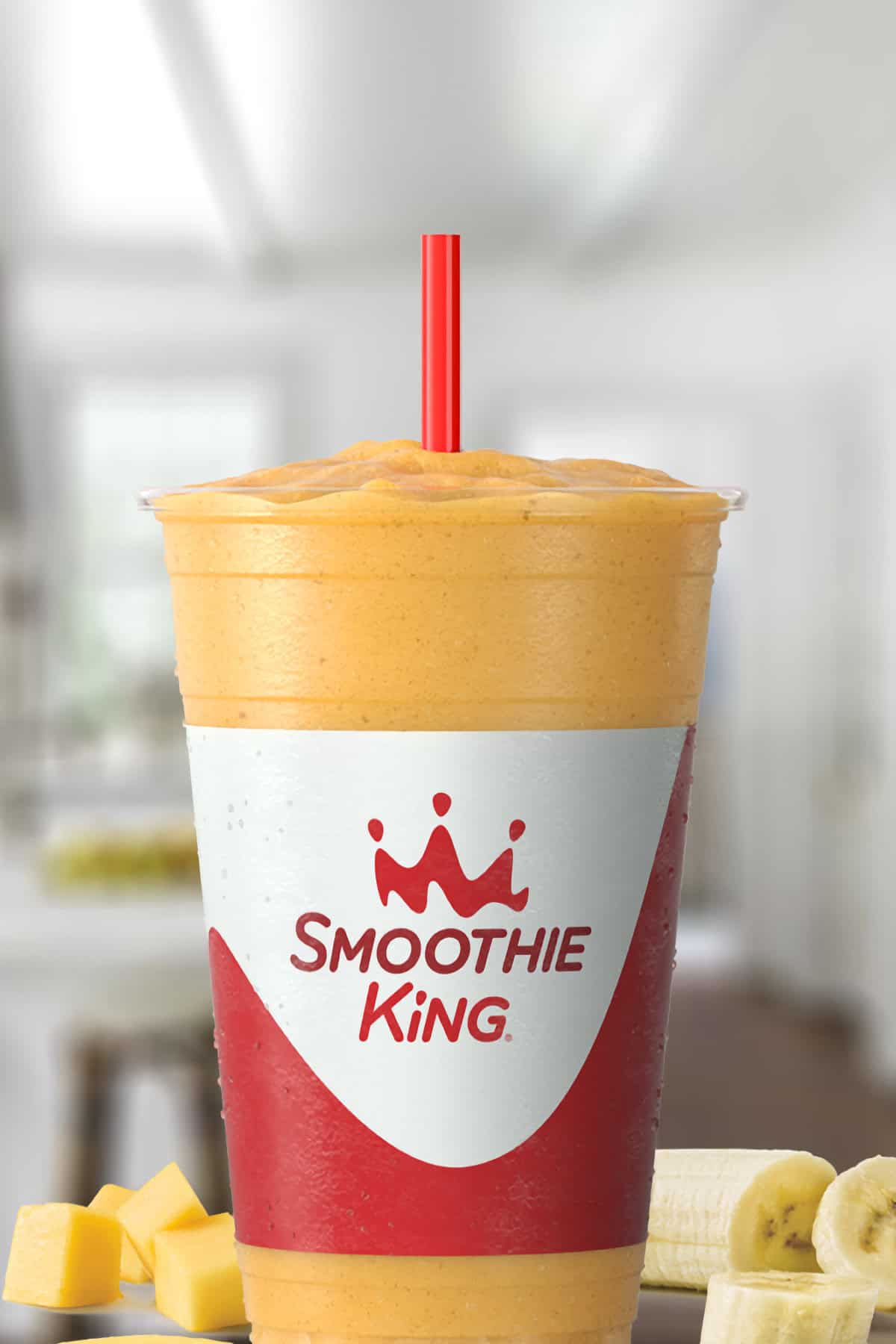 Smoothie King Passion Passport smoothie in a glass, on my kitchen counter, surrounded by fresh papaya chunks and bananas.