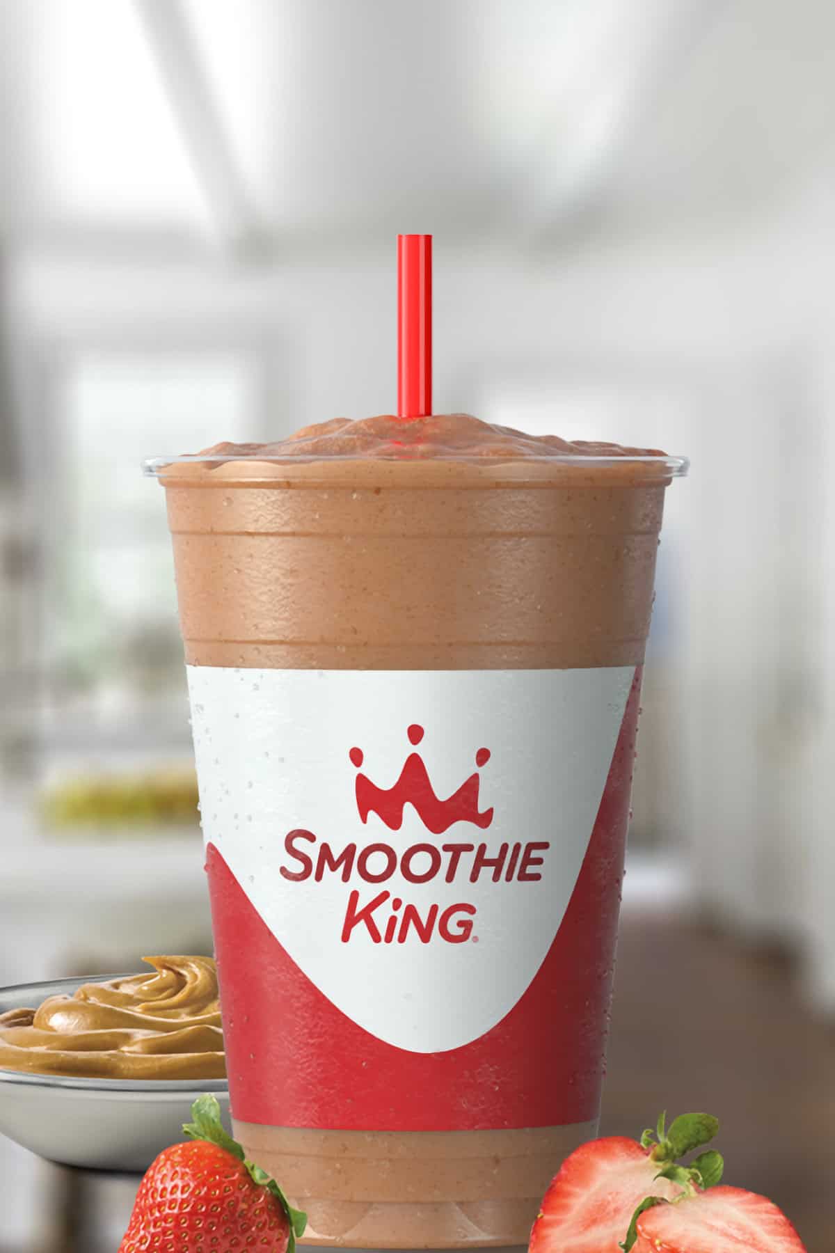 Smoothie King Peanut Power Plus Strawberry smoothie in a glass, on my kitchen counter, surrounded by creamy peanut butter and fresh strawberries.