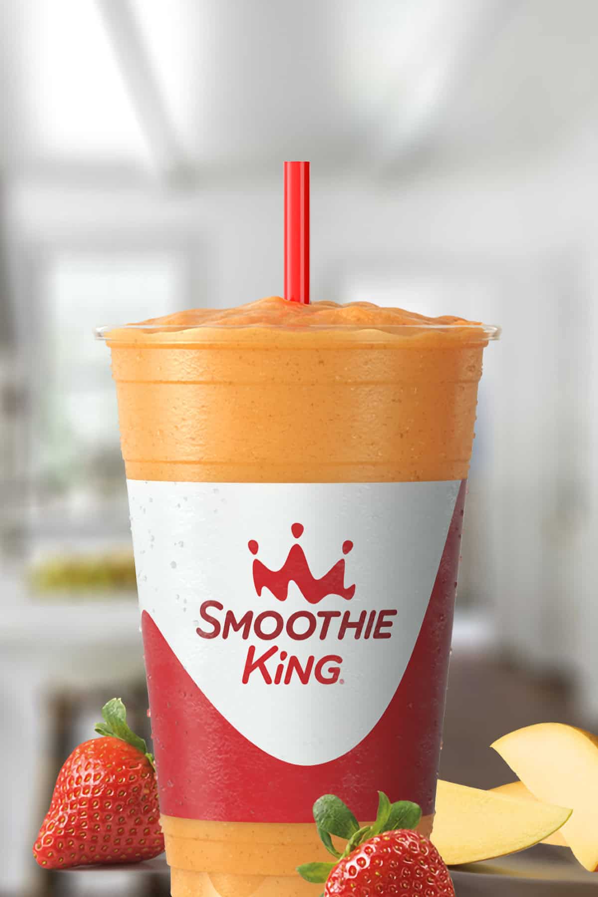 Smoothie King Pure Recharge Mango Strawberry smoothie in a glass, on my kitchen counter, surrounded by fresh strawberries and mangoes.