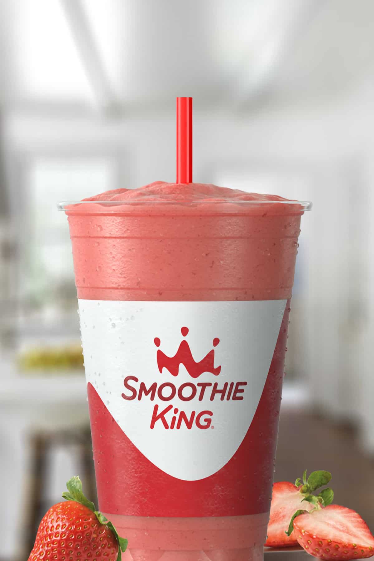 Smoothie King Pure Recharge Strawberry smoothie in a glass, on my kitchen counter, surrounded by fresh strawberries.