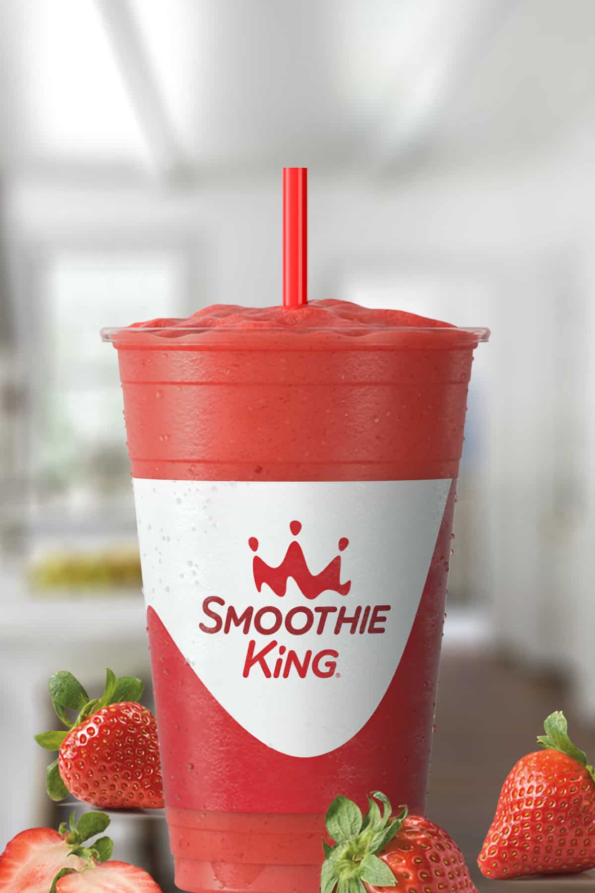 Smoothie King Strawberry X-Treme smoothie in a glass, on my kitchen counter, surrounded by fresh strawberries.