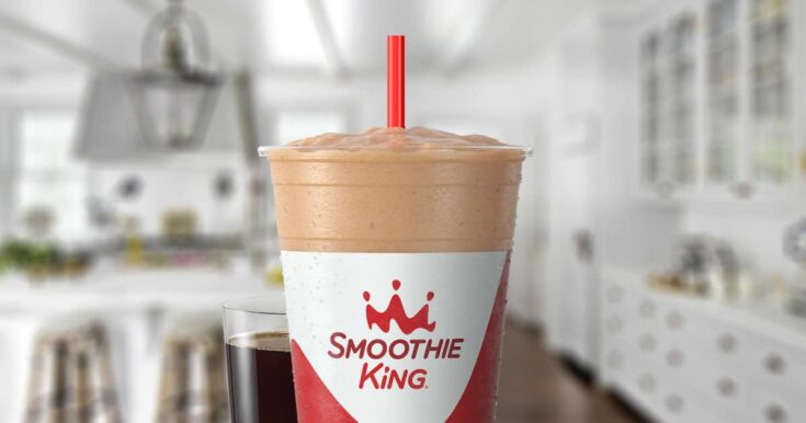 Smoothie King The Activator Recovery Espresso smoothie in a glass, on my kitchen counter, surrounded by coffee beans and a double shot of espresso.