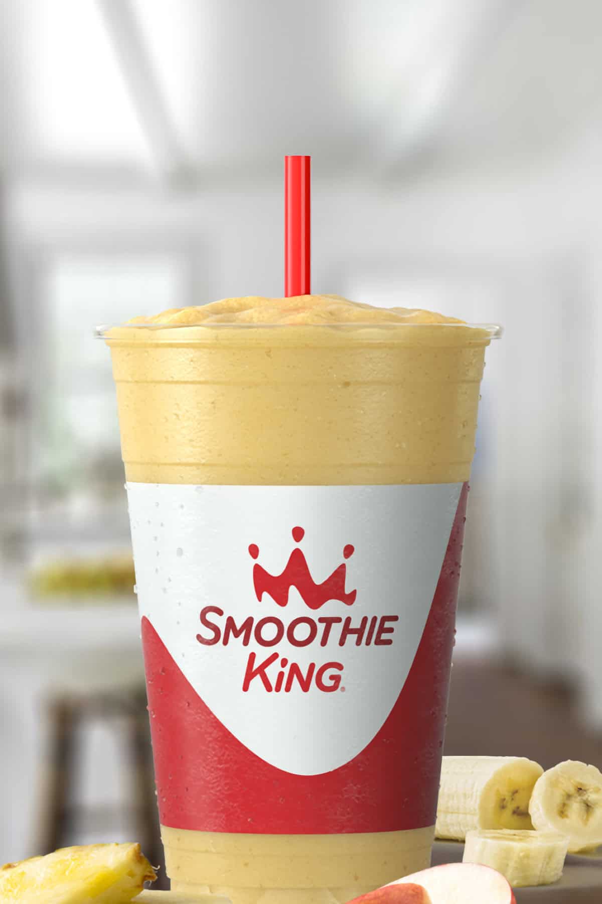 Smoothie King The Activator Recovery Pineapple smoothie in a glass, on my kitchen counter, surrounded by pineapples and sliced bananas.