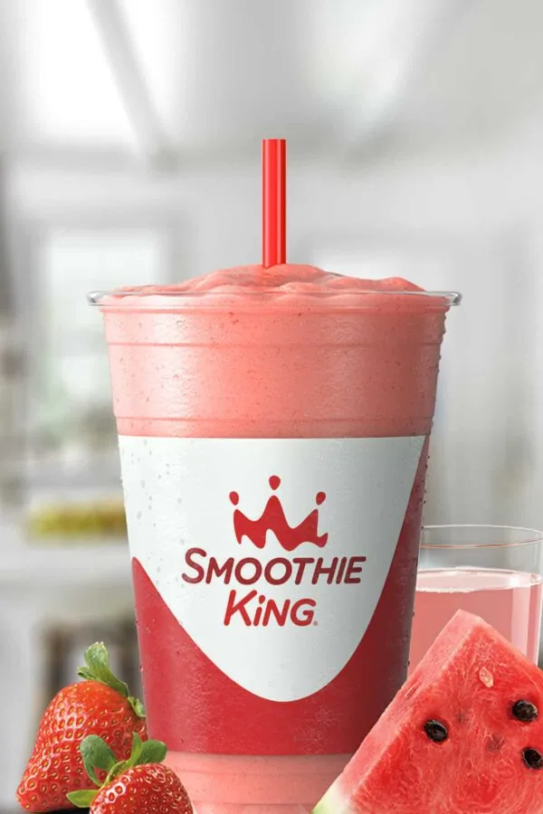 Smoothie King X-Treme Watermelon smoothie in a glass, on my kitchen counter, surrounded by fresh strawberries and watermelon slices.