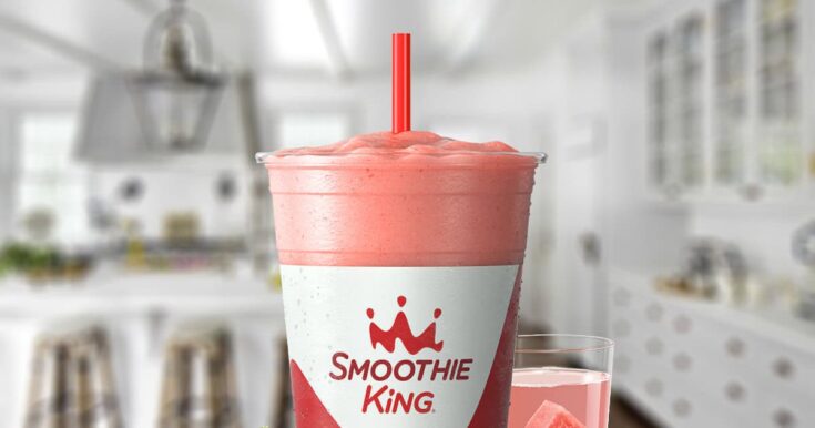 Smoothie King X-Treme Watermelon smoothie in a glass, on my kitchen counter, surrounded by fresh strawberries and watermelon slices.