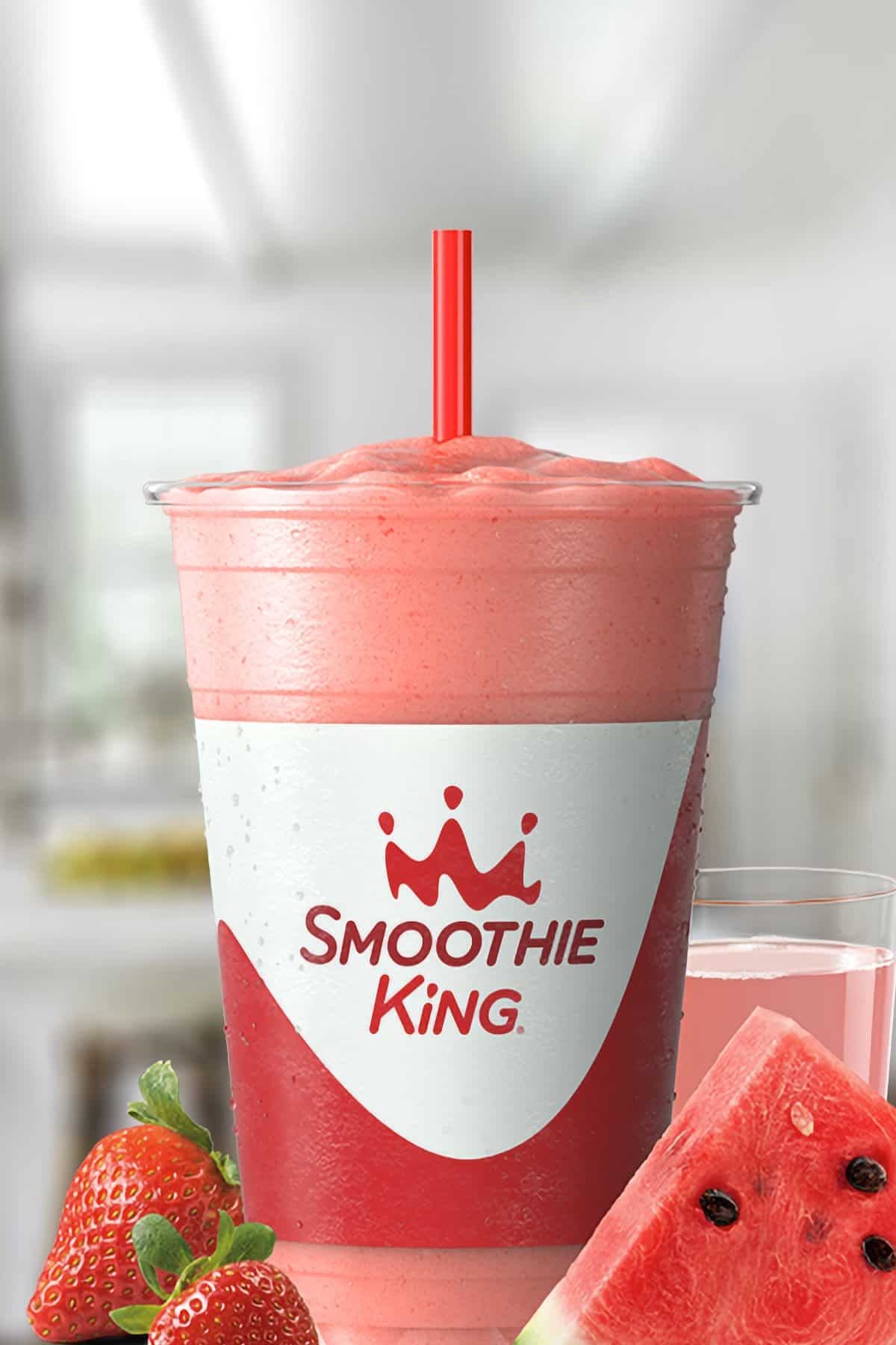 Smoothie King X-Treme Watermelon smoothie in a glass, on my kitchen counter, surrounded by fresh strawberries and watermelon slices.