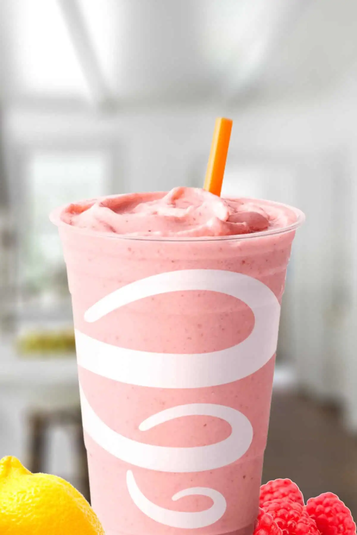 Jamba Juice Pink Star smoothie in a glass, on my kitchen counter, surrounded by lemon slices and fresh raspberries.