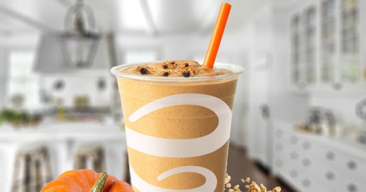 Jamba Juice Pumpkin Pie Crunch smoothie in a glass, on my kitchen counter, surrounded by pumpkins and granola.