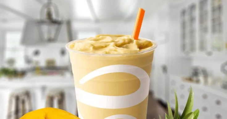 Jamba Juice Smooth Talkin' Mango smoothie in a glass, on my kitchen counter, surrounded by fresh mango and pineapple.