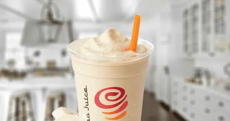 Jamba Juice Soy PB + Banana Protein smoothie in a glass, on my kitchen counter, surrounded by banana slices and peanuts.