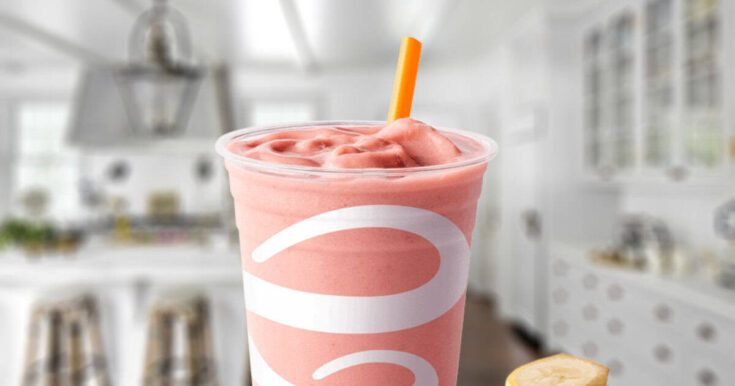 Jamba Juice Soy Protein Berry Workout smoothie in a glass, on my kitchen counter, surrounded by banana slices and strawberries.