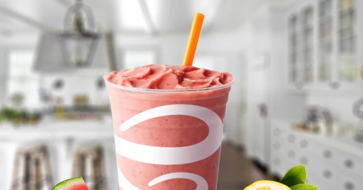 Jamba Juice Watermelon Lemonade smoothie in a glass, on my kitchen counter, surrounded by fresh watermelon and lemon slices.