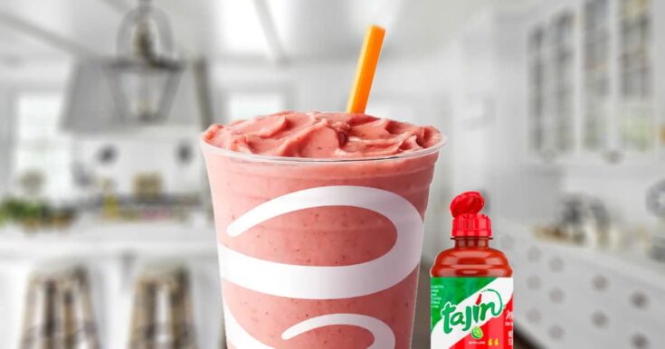 Jamba Juice Watermelon Tajin smoothie in a glass, on my kitchen counter, surrounded by fresh watermelon and Tajin mild hot sauce.