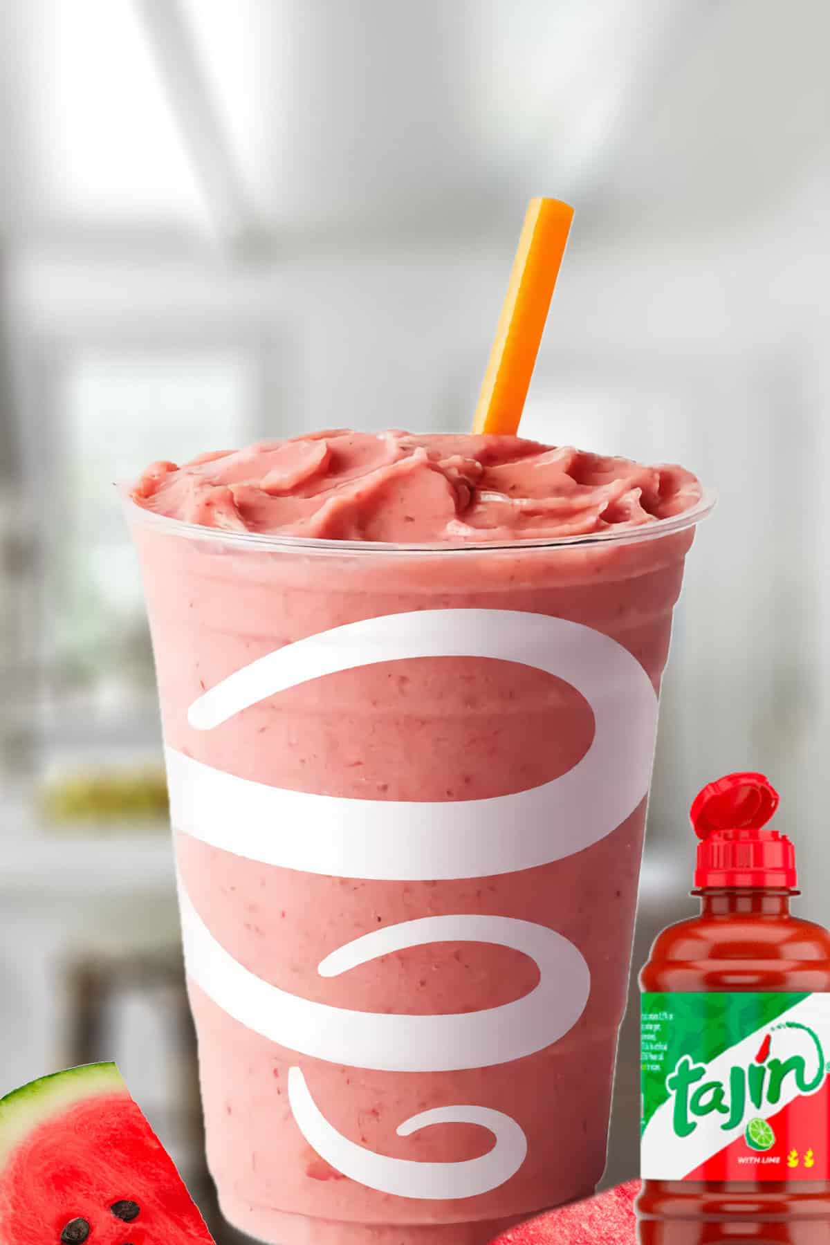 Jamba Juice Watermelon Tajin smoothie in a glass, on my kitchen counter, surrounded by fresh watermelon and Tajin mild hot sauce.