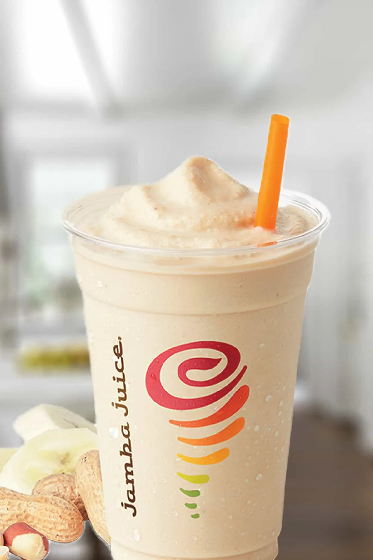 Jamba Juice Whey PB + Banana Protein smoothie in a glass, on my kitchen counter, surrounded by banana slices and peanuts.