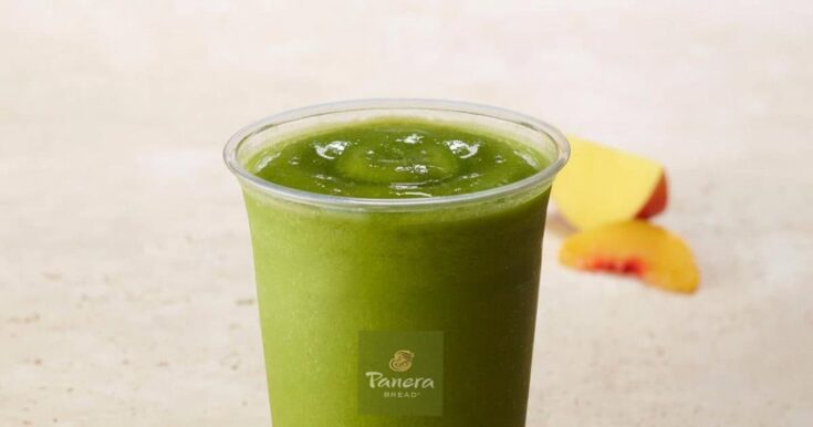 Panera Green Passion smoothie in a glass, on my kitchen counter, surrounded by fresh mango slices.