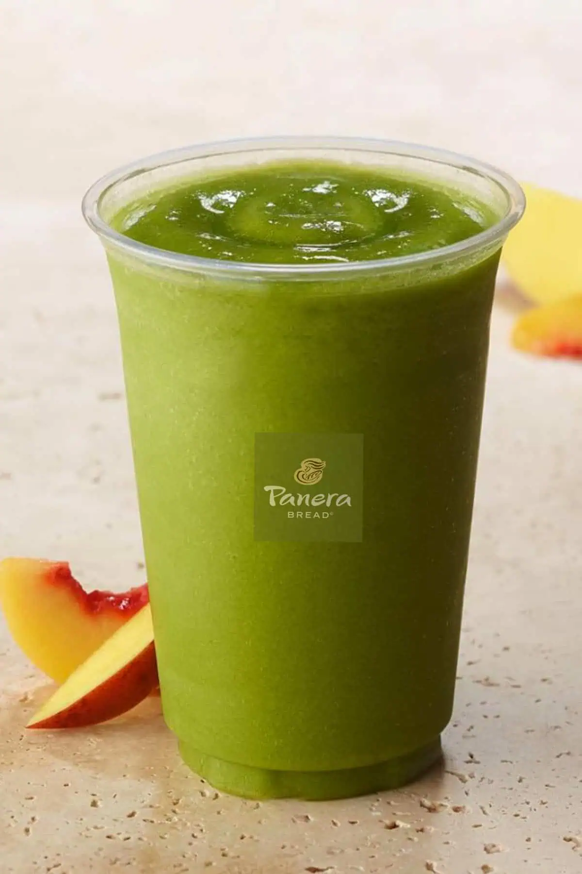 Panera Green Passion smoothie in a glass, on my kitchen counter, surrounded by fresh mango slices.