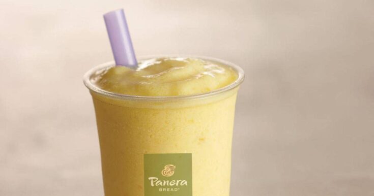 Panera Mango smoothie in a glass, on my kitchen counter, surrounded by fresh mango slices.