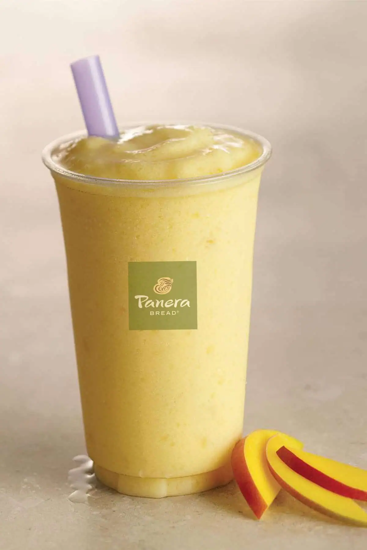 Panera Mango smoothie in a glass, on my kitchen counter, surrounded by fresh mango slices.