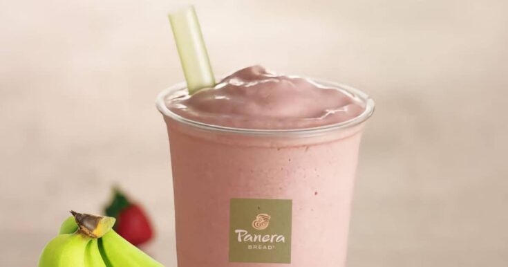 Panera Strawberry Banana smoothie in a glass, on my kitchen counter, surrounded by fresh strawberries and bananas.