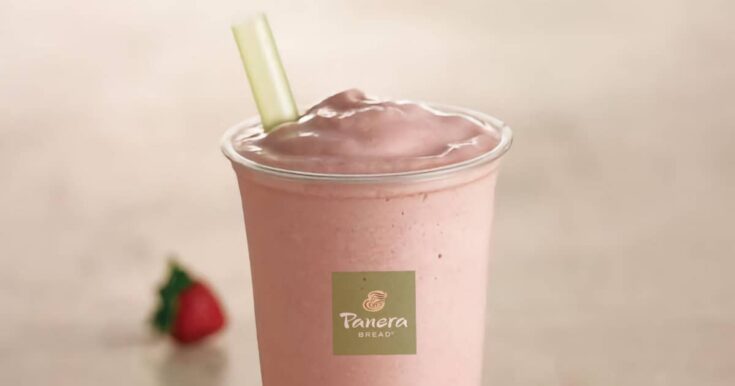 Panera Strawberry smoothie in a glass, on my kitchen counter, surrounded by fresh strawberries.