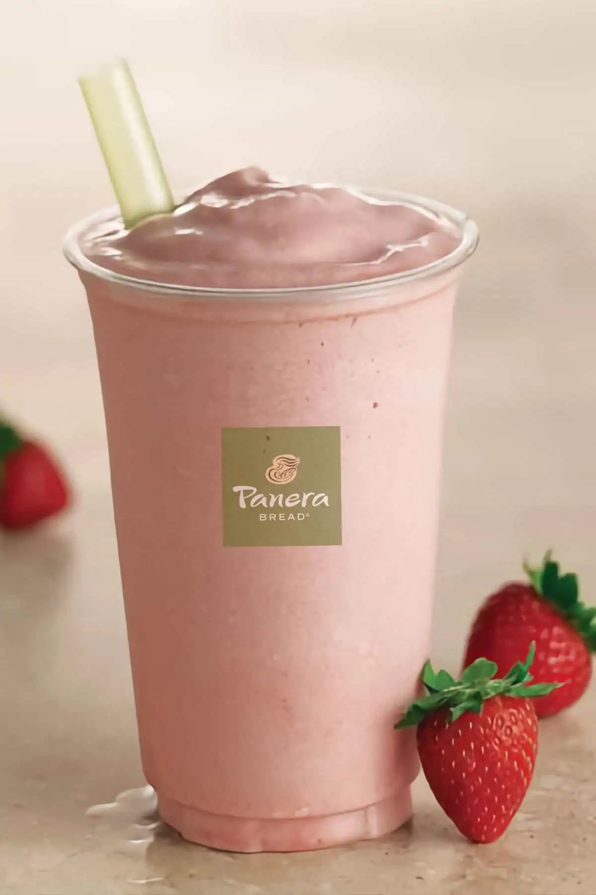 Panera Strawberry smoothie in a glass, on my kitchen counter, surrounded by fresh strawberries.