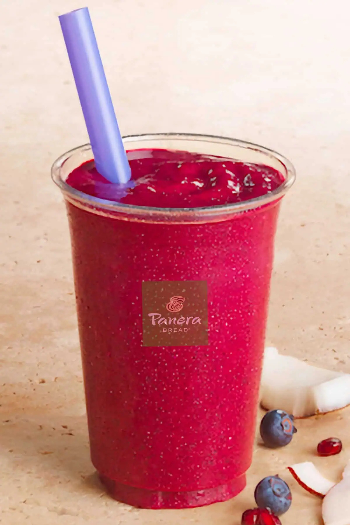 Panera Blueberry Pomegranate Vegan smoothie in a glass, on my kitchen counter, surrounded by fresh blueberries, pomegranate seeds, and coconut.