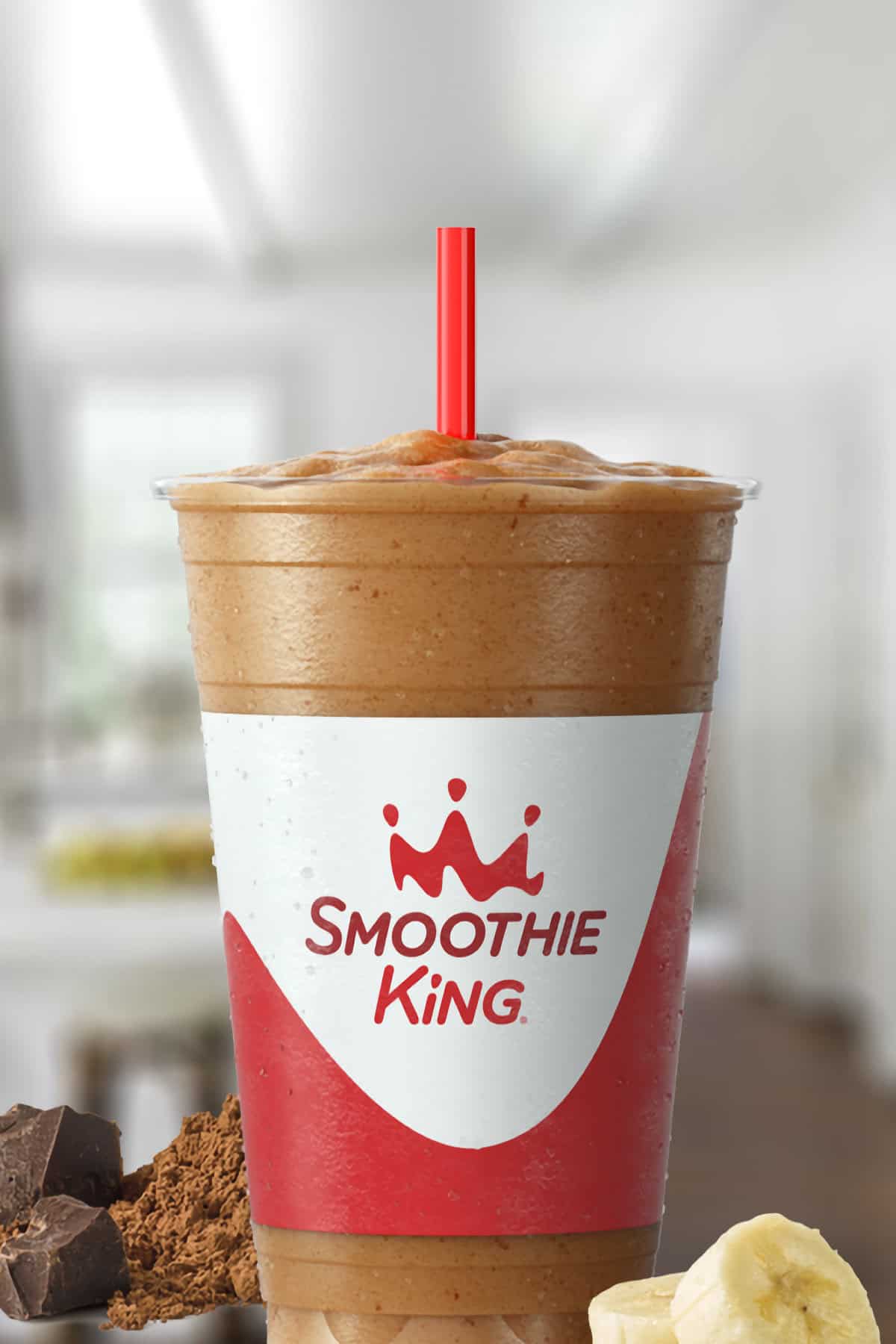 Smoothie King Power Slim Chocolate smoothie in a glass, on my kitchen counter, surrounded by cacao and banana slices.