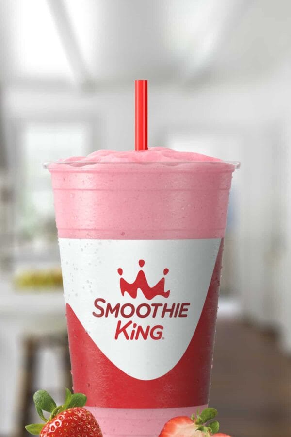Smoothie King Power Slim Strawberry smoothie in a glass, on my kitchen counter, surrounded by fresh strawberries.