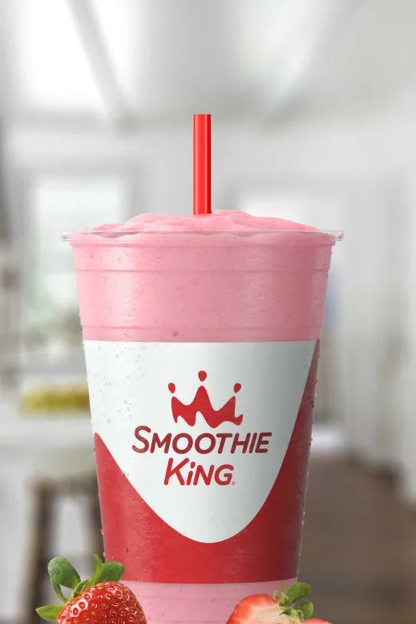 Smoothie King Power Slim Strawberry smoothie in a glass, on my kitchen counter, surrounded by fresh strawberries.