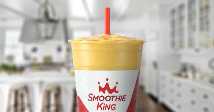 Smoothie King Slim-N-Trim Vanilla smoothie in a glass, on my kitchen counter, surrounded by fresh sliced bananas.