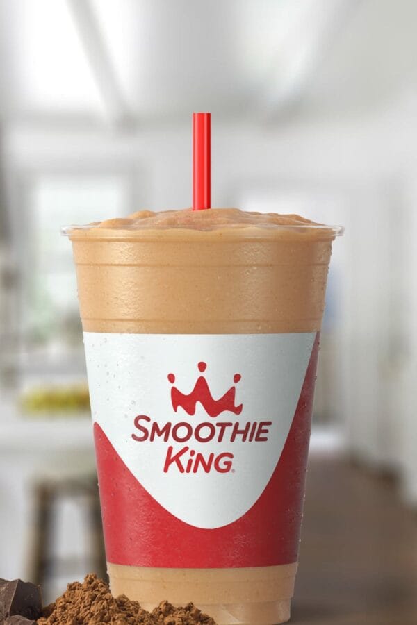 Smoothie King Gladiator Chocolate smoothie in a glass, on my kitchen counter, surrounded by blueberries.