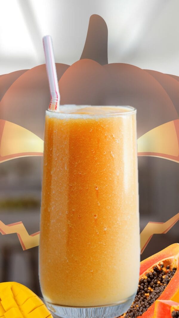Candy Corn Halloween smoothie in a glass, on my kitchen counter, surrounded by fresh tropical fruit.